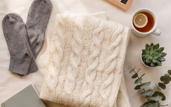 Cozy flat lay of Christmas gifts for an elderly parent in assisted living: cable knit throw, grip socks, family photo frame, tea, and reading glasses